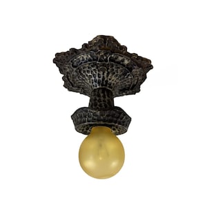 May include: A bronze-colored ceiling light fixture with a textured, ornate design. The fixture has a bulb with a yellow tint. The light is designed to be mounted on a ceiling and provides illumination.