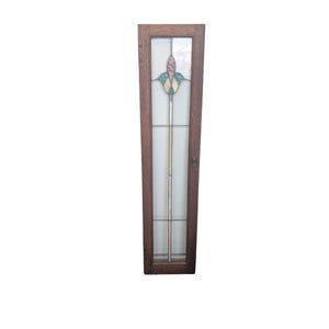 May include: A tall, rectangular wooden door with a stained glass panel. The panel features a floral design with pink, green, and yellow accents. The door has a dark brown frame and a small metal handle.