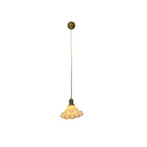 May include: A vintage-style pendant light fixture with a ruffled, off-white glass shade. The fixture has a brass-colored canopy and a twisted cord. The light is suspended from the ceiling, showcasing a classic design.