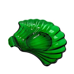 May include: A vibrant green glass decorative bowl with a seashell design. The bowl features a central circular indentation and a scalloped edge. The glass has a glossy finish with black accents, creating a striking contrast. The bowl is designed to resemble a seashell.