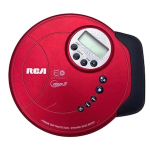 Pode incluir: Leitor de CD MP3 RCA vermelho com uma pega preta. O leitor tem um visor digital e botões de controlo. O texto no leitor diz "RCA", "Ex", "ESP Xtreme", "mp3", "Xtreme Skip Protection - Dynamic Bass Boost".