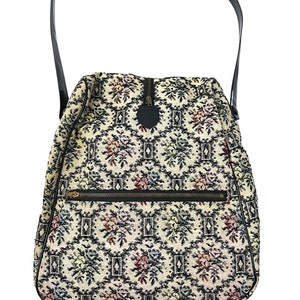 Könnte beinhalten: Eine Vintage-Duffel-Tasche im Tapisserie-Stil mit einem schwarzen Lederriemen und einem Reißverschluss. Die Tasche hat ein florales Muster in den Farben Schwarz, Weiß, Rot und Blau.
