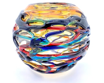 May include: A round glass vase with a colorful, abstract design. The vase is made of clear glass with black, red, blue, and yellow stripes. The stripes are arranged in a random pattern, creating a unique and eye-catching design.