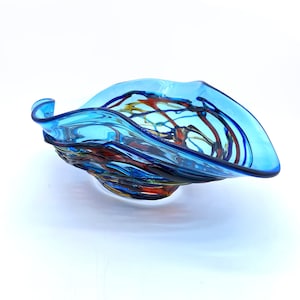 May include: A blue glass bowl with a wavy edge and colourful swirls of red, yellow, and blue glass.