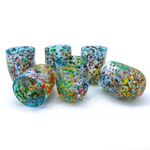 Könnte beinhalten: Sechs bunte, gesprenkelte Glasbecher. Jeder Becher hat ein einzigartiges Muster aus roten, gelben, grünen und blauen Punkten auf klarem Hintergrund. Die Gläser haben eine abgerundete Form und einen türkisfarbenen Rand.