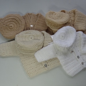 May include: A set of four crocheted baby sweaters and hats in cream and white. The sweaters have button closures and the hats are simple and round.