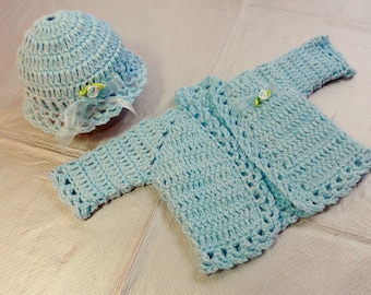May include: A light blue crocheted baby hat and cardigan set with white trim and a small flower embellishment.