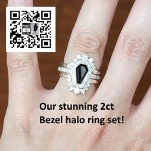 May include: A three-piece ring set featuring a black gemstone in a coffin-shaped setting surrounded by a halo of clear stones. The set includes a thin band and a wider band with a textured finish.
