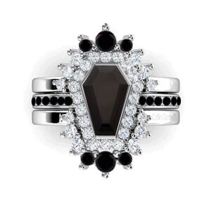 May include: A silver ring set with a black coffin-shaped gemstone surrounded by a halo of smaller white and black gemstones.