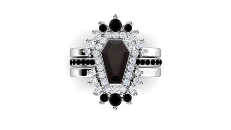 May include: A silver ring set with a black coffin-shaped gemstone surrounded by a halo of smaller white and black gemstones.