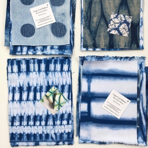 May include: Four fabric swatches with indigo dye patterns. One swatch features large dark blue polka dots, another has a web-like design, a third has vertical lines, and the last has horizontal stripes. Each swatch has a frayed edge.