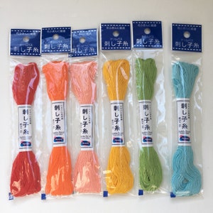 May include: Six spools of embroidery floss in various colors, including red, orange, pink, yellow, green, and blue. Each spool is labeled "Olympus" and "Sashiko Thread" in Japanese characters. The spools are packaged in clear plastic bags with a blue header that reads "Olympus Sashiko Thread" in Japanese characters.