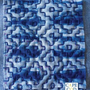 May include: A close-up of a blue and white fabric with a geometric pattern. The fabric is stitched together in a grid-like pattern. The fabric is labeled "Cape Cod Shibori".