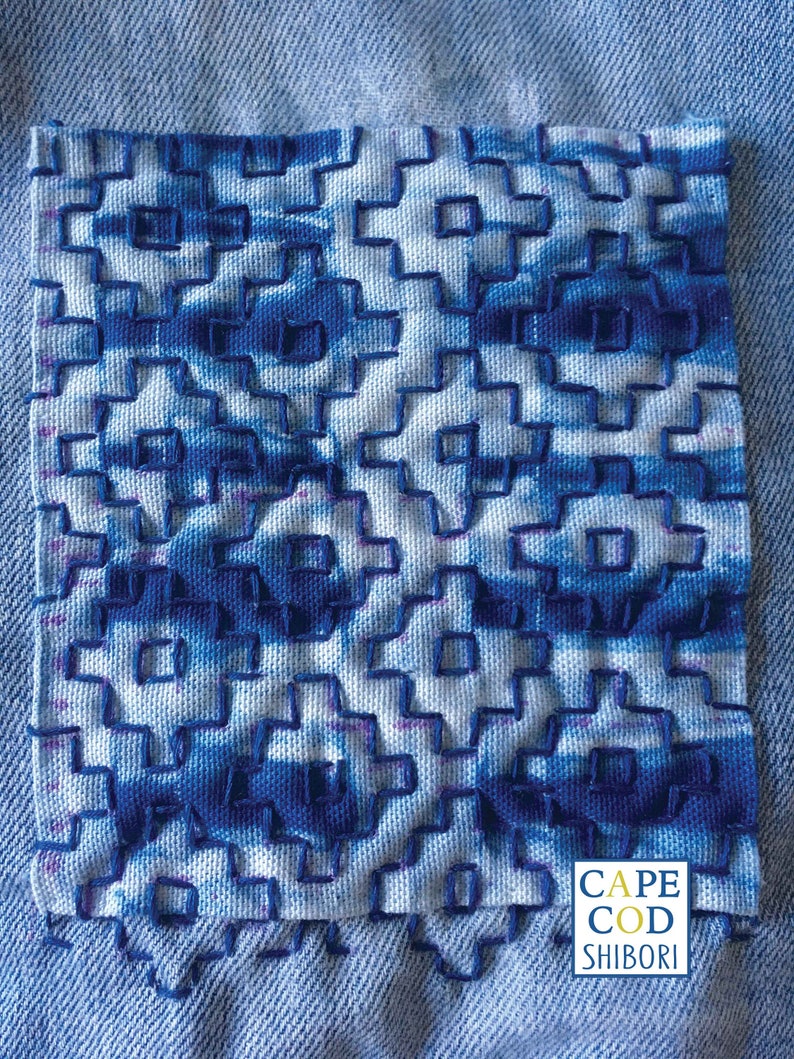 May include: A close-up of a blue and white fabric with a geometric pattern. The fabric is stitched together in a grid-like pattern. The fabric is labeled "Cape Cod Shibori".