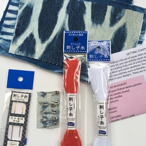 May include: A sashiko embroidery kit with two spools of thread, one red and one white, a pack of needles, safety pins, and two denim patches. The packaging is labeled in Japanese with the text "Sashiko Thread" and "Sashiko Needle".