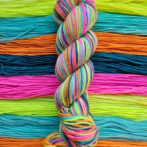 Könnte beinhalten: Ein Garnstrang mit einem lebendigen, mehrfarbigen Muster aus Neonpink, hellem Limettengrün, Türkis und Orange, der vertikal vor einem Hintergrund aus horizontalen Garnsträngen in der gleichen Farbpalette präsentiert wird.