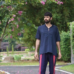 May include: A man wearing a dark blue shirt and dark blue pants with colorful embroidered details. He is standing on a paved path with pink flower petals scattered on the ground.
