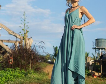 May include: A woman wearing a teal blue maxi dress with a loose, flowing fit. She is standing on a wooden platform with a green grassy background.