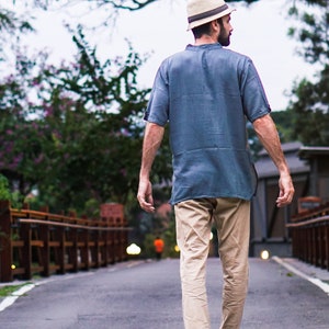 May include: A man wearing a light blue short-sleeved shirt, khaki pants, and a straw hat walks down a paved path.