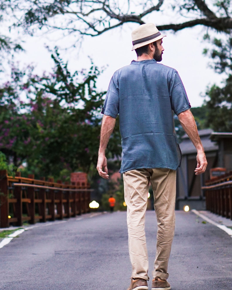 May include: A man wearing a light blue short-sleeved shirt, khaki pants, and a straw hat walks down a paved path.