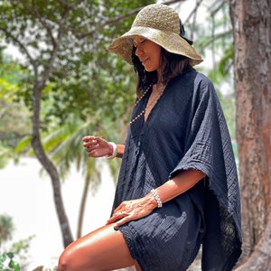 K&ouml;nnte beinhalten: Eine Frau tr&auml;gt eine schwarze, lockere Baumwoll-Kaftan mit weiten, flie&szlig;enden &Auml;rmeln. Sie tr&auml;gt einen Strohhut mit schwarzem Band und eine Perlenkette.
