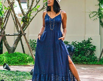 Puede incluir: Un vestido largo azul marino con corpiño de encaje, tirantes finos y una abertura alta. El vestido presenta un dobladillo con volantes con un diseño calado y se combina con un sombrero blanco y joyas doradas. El vestido tiene bolsillos.