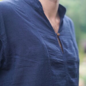 May include: A dark blue, long-sleeved shirt with a v-neck and a single button closure.