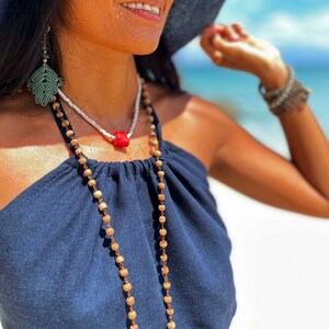 May include: A woman wearing a navy blue halter top with a long beaded necklace and a coral pendant. She is also wearing a pair of green leaf earrings.