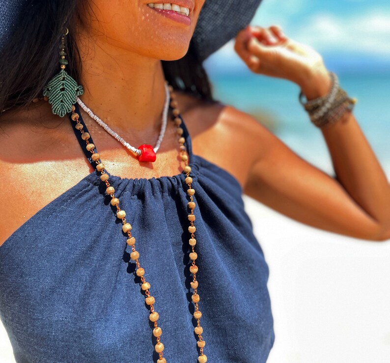 May include: A woman wearing a navy blue halter top with a long beaded necklace and a coral pendant. She is also wearing a pair of green leaf earrings.