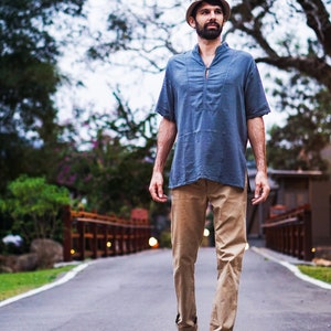 May include: A man wearing a blue short-sleeved shirt, khaki pants, and a light brown fedora hat walks down a paved path.