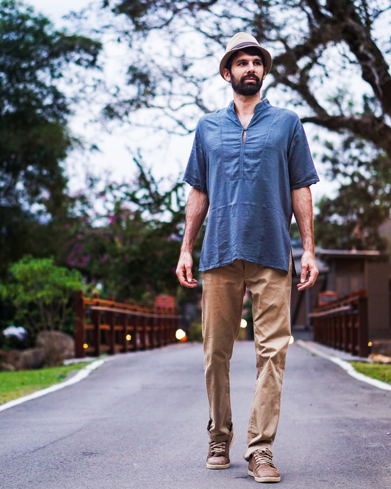May include: A man wearing a blue short-sleeved shirt, khaki pants, and a light brown fedora hat walks down a paved path.