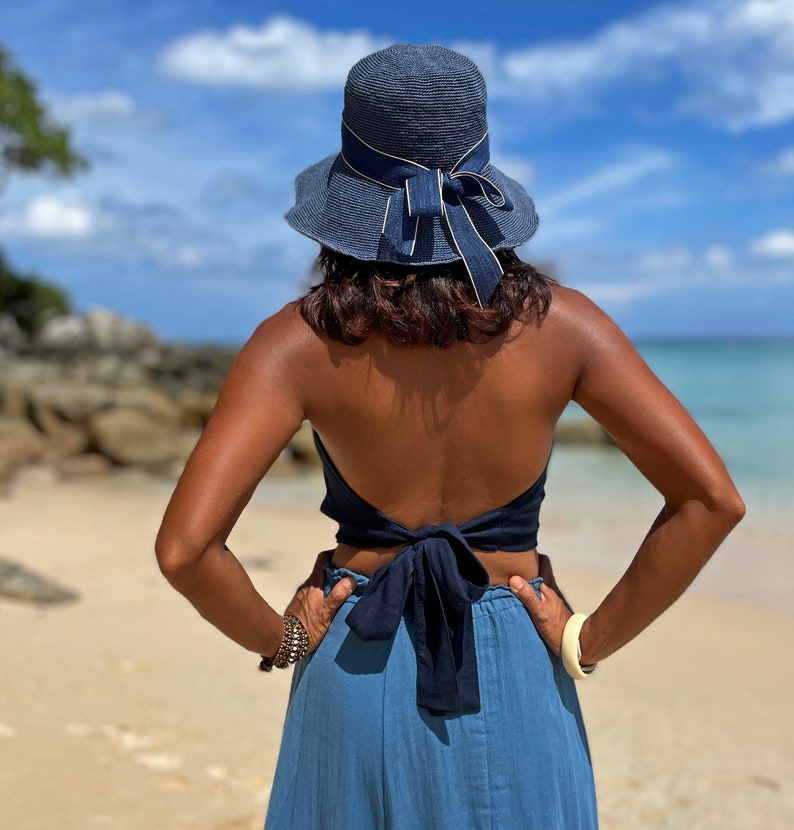 May include: A woman wearing a blue denim skirt and a blue halter top tied in a bow at the back. She is wearing a blue sun hat with a gold ribbon.