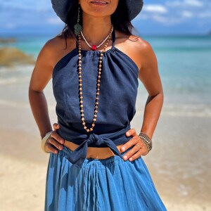 May include: A woman wearing a navy blue halter top with a knotted front and a matching blue skirt. She is wearing a long beaded necklace with a red accent.
