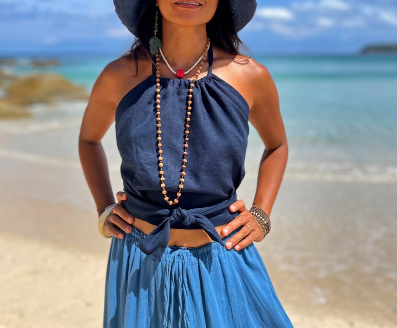 May include: A woman wearing a navy blue halter top with a knotted front and a matching blue skirt. She is wearing a long beaded necklace with a red accent.