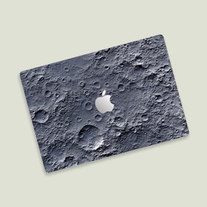 May include: A dark grey laptop skin with a moon-like surface and a white Apple logo.