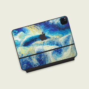 Puede incluir: Un iPad Pro de Apple con una llamativa funda abstracta que presenta un diseño dinámico de olas oceánicas en tonos azules, blancos y amarillos. La funda cubre la parte trasera y los bordes del dispositivo, con el logotipo de Apple visible.