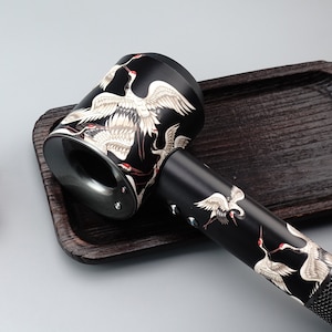 May include: Black hair dryer with a white and black crane design. The dryer has a nozzle and a handle.