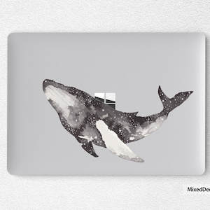 May include: A gray laptop skin with a watercolor illustration of a whale with a galaxy pattern. The whale is swimming towards the right side of the image. The whale has a white underbelly and a black back with white stars. The whale is swimming through a window.