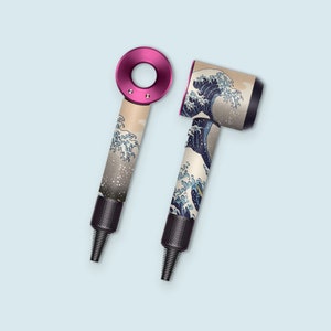 Może przedstawiać: Dwa suszarki do włosów w różowo-czarnym kolorze. Jedna suszarka ma wzór fal w kolorze białym i niebieskim, druga ma różową rączkę i wzór fal w kolorze białym i niebieskim na cylindrze.