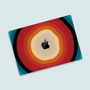 Puede incluir: Un diseño abstracto colorido con círculos concéntricos en tonos de rojo, naranja, amarillo y azul. El centro del diseño presenta un logotipo de Apple negro.