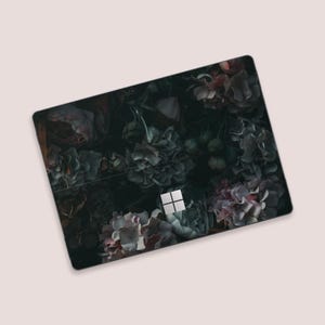 May include: A black laptop adorned with a floral pattern of dark roses and other flowers in pink, grey, and green hues. The laptop features a Microsoft logo in the centre.