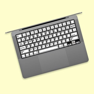 Puede incluir: Un ordenador portátil gris con un teclado negro. Las teclas tienen etiquetas escritas a mano.
