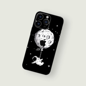 May include: Black iPhone case with a white astronaut holding onto a moon-shaped balloon with a bite taken out of it. The background is black with white stars.