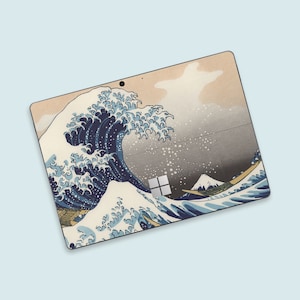 Può includere: Una skin per laptop con l'iconica opera d'arte giapponese "La Grande Onda di Kanagawa". Il design mostra una grande onda stilizzata nei toni del blu e del bianco, con il Monte Fuji sullo sfondo. La skin è applicata a un laptop.