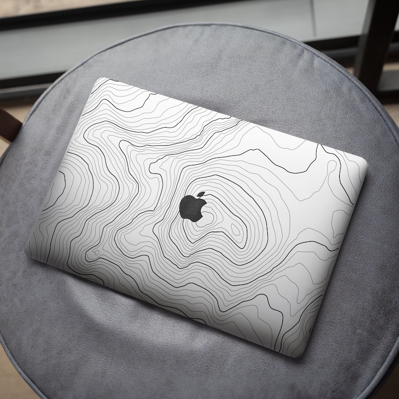 May include: White laptop computer with a black and white topographic map design. The laptop has an apple logo on the lid.