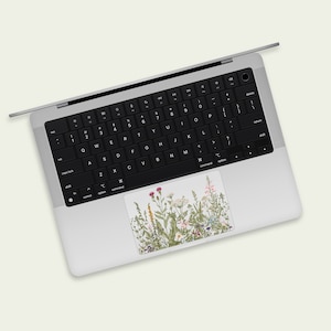 May include: A silver laptop computer with a black keyboard and a floral sticker on the trackpad. The sticker features a variety of wildflowers in shades of pink, purple, and white.