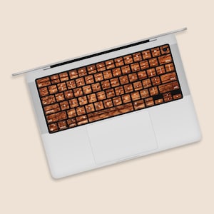Może przedstawiać: Srebrny laptop z drewnianą nakładką na klawiaturę. Klawiatura ma białe oznaczenia na klawiszach.