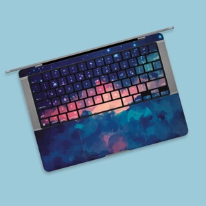 Pode incluir: Um computador portátil com um design abstrato colorido na tampa e no teclado. O design apresenta tons de azul, roxo e rosa, que se assemelham a uma pintura em aquarela.