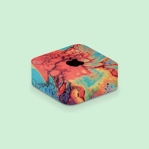 May include: A colorful, abstract patterned computer case. The case features a vibrant mix of red, orange, blue, and yellow hues, with a black Apple logo on top. The design resembles a fluid art style.