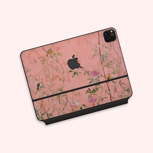 May include: A pink tablet case featuring a floral design with birds and the Apple logo. The case has a black border and a textured, vintage-style background. The design includes pink flowers and green leaves.